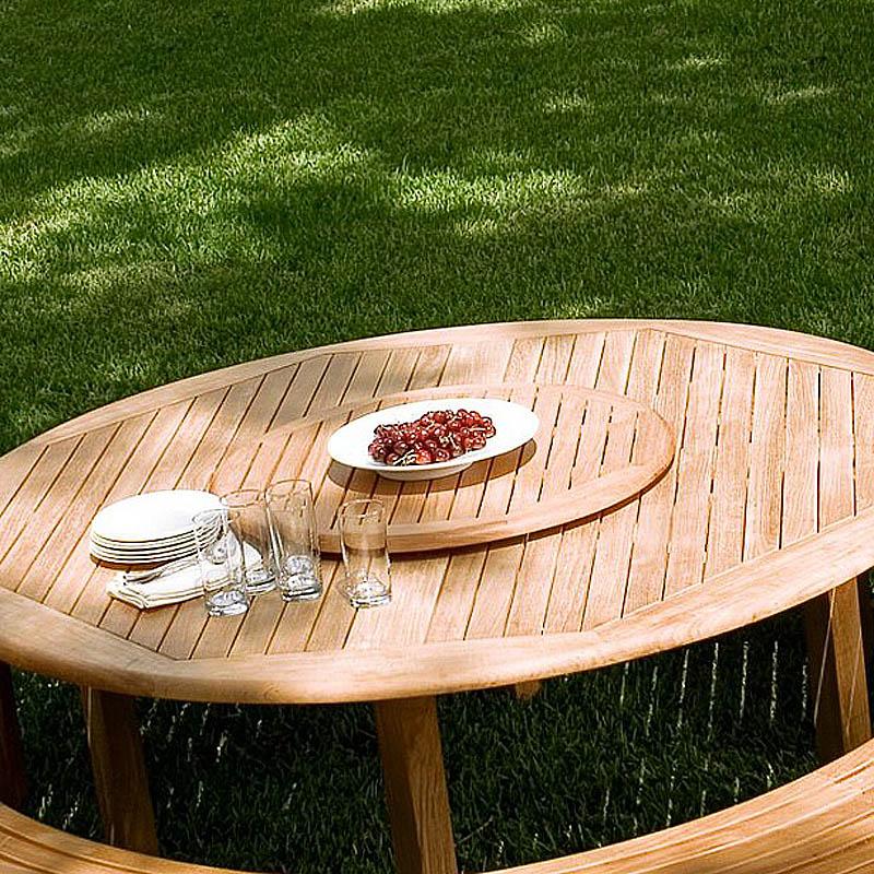 alt="18705 round 32 inch teak lazy susan in round dining table with bowl of grapes on table with four glasses plates and napkins on grass lawn"