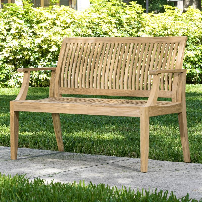 alt="13810 Laguna 4 foot Teak Bench angled on concrete walkway with bushes in background"