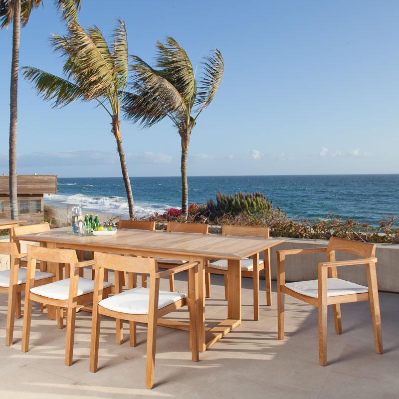 alt="12901ST Horizon Dining Chair with  Horizon 9 piece Teak Dining Set on concrete patio overlooking ocean with condo on left palm trees and blue sky background"