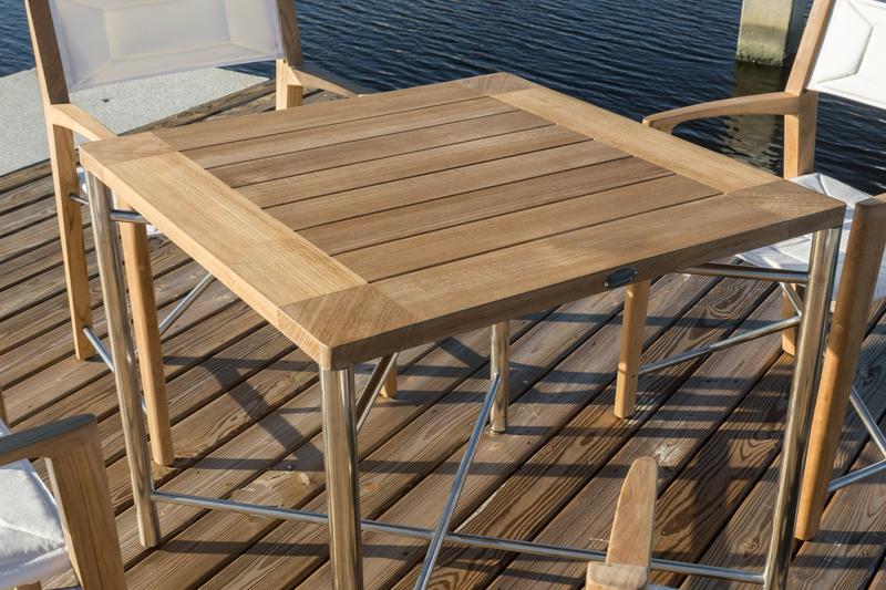 alt="25815 Odyssey 32 inch square teak and stainless steel dining table on boat dock with marina view in background"
