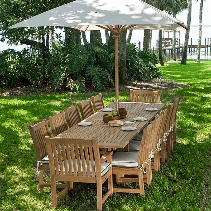 alt="70017 Grand Veranda 13 piece dining set with optional seat cushions and optional market umbrella bowl of apples a plate of bread wood bowls plates on grass with dock and lake background"