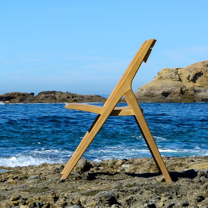 alt="70474 Surf Barbuda folding side chair on sandy beach left side facing ocean with rocks and blue sky background"