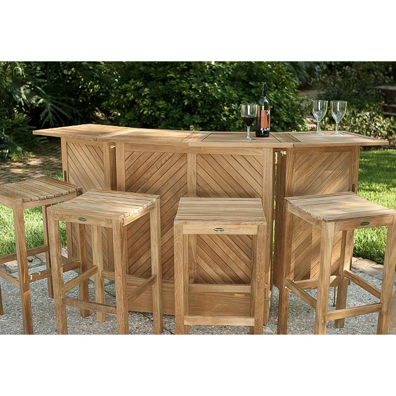 alt=" 70084 somerset teak five piece bar set showing three wine glasses and wine bottle on top with stone patio a grass area paver walkway and lush tropical plants in background"