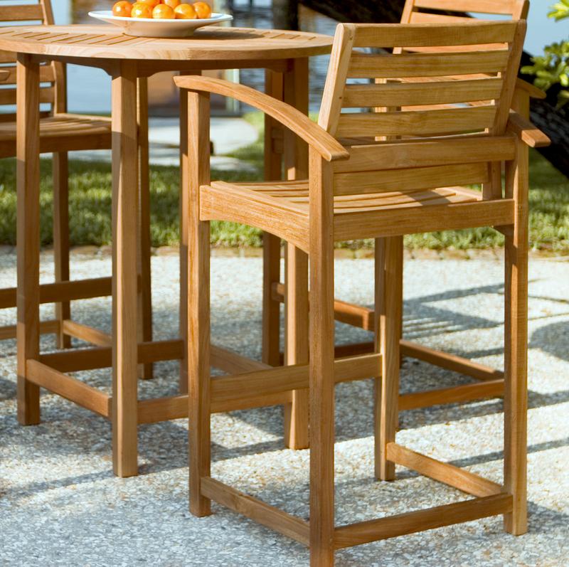 alt="12466 Somerset Teak Bar Stool rear angled and table with bowl oranges on concrete patio overlooking lake in background"