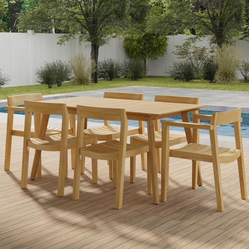 alt="70525 Surf Horizon 7 pc Dining Set of a Surf Teak 60 inch Rectangular Table side angled on patio in front of a pool with grass and landscaping plants and trees and white fence in the background"