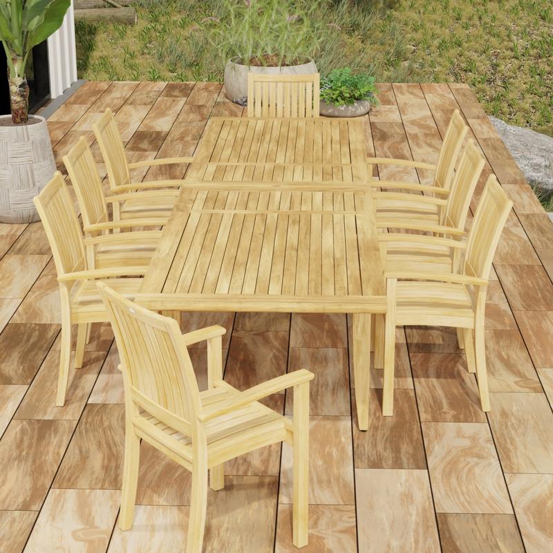 alt="70774 Laguna Sussex 9 pc Teak Dining Set of Grand Laguna Table and 8 Sussex Armchairs in end view on patio with potted plants and grass area in background"