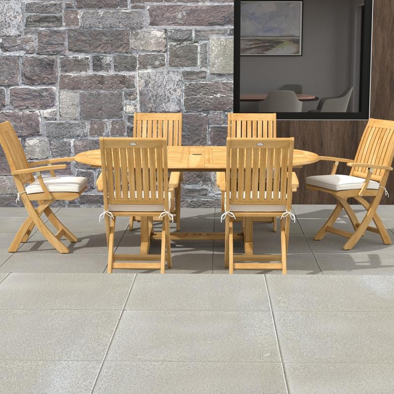 alt="70368 Martinique Oval Barbuda Chair 7 pc Dining Set of Martinique Oval Table and 6 Barbuda Teak Arm Chairs in side view on patio with stone house in the background"