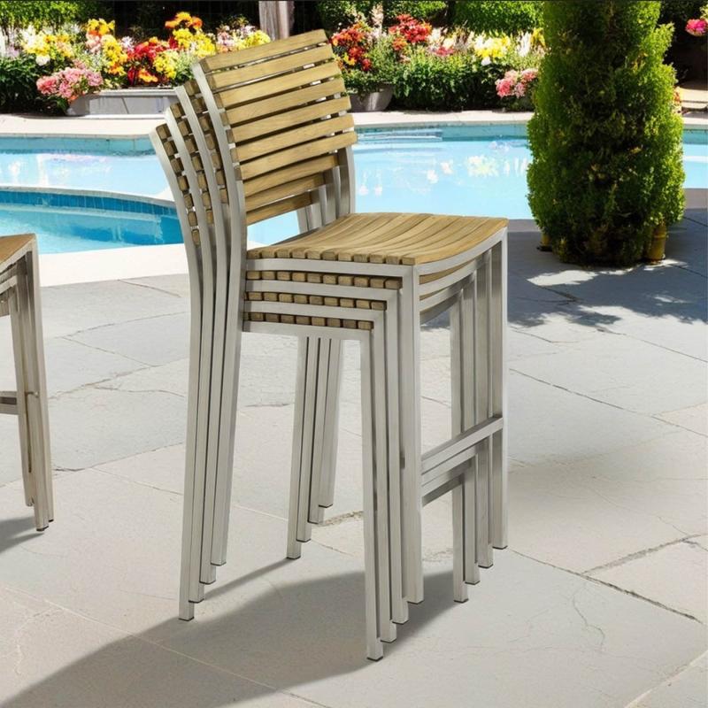 alt="21510ST Vogue Bar Stool stacked 4 high in angled side view on a pool deck with pool and landscaping trees and plants in background"