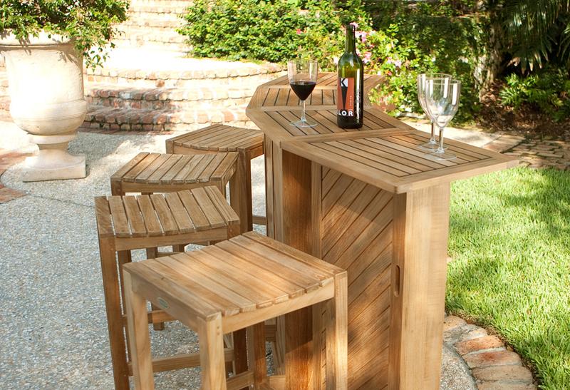 alt=" 17112 Somerset teak bar and stools bar fully opened showing three wine glasses and wine bottle on bar top displayed on patio with potted plants stone steps vegetation in background "