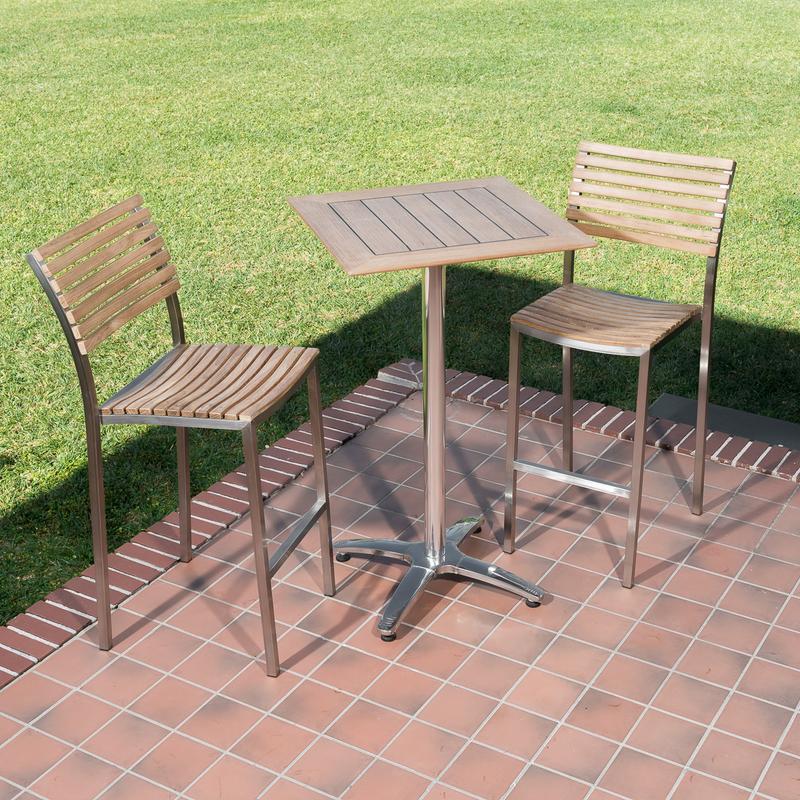 alt=" 70673 Vogue teak and stainless steel High Bar Set of 2 barstools and 24 inch square teak table angled aerial view on paver patio with grass lawn in background"
