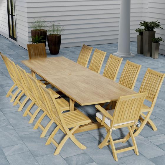  70059 Grand Barbuda 13 pc Teak Dining Set angled end view on patio with optional seat cushions and 6 potted plants against the house wall in the background
