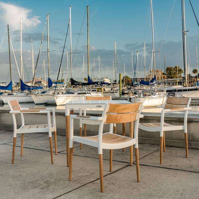 alt="22916 Bloom Dining chair of 4 chairs around Bloom Square table on concrete dock with boats in marina and blue sky background"