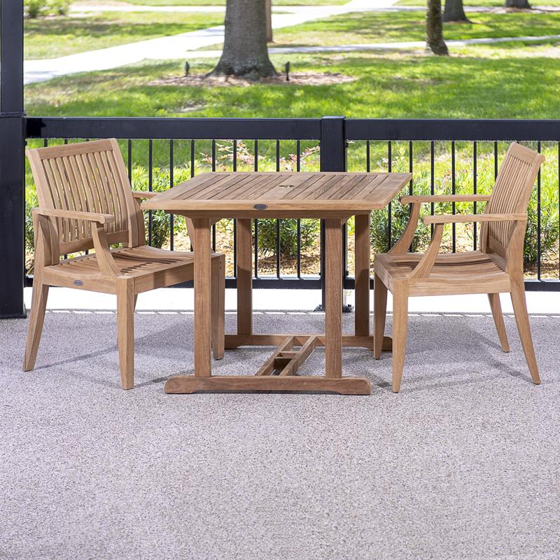 alt="70301 Laguna 3 piece teak Dining Set of a 36 inch square dining table and 2 teak dining armchair on concrete patio against a black railing with grass lawn and trees in background"