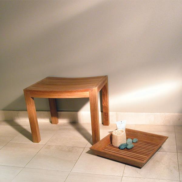 alt="17420 Pacifica teak Vanity Tray with loofah black stones and lotion bottle on tiled indoor floor up against wall beside shower bench"