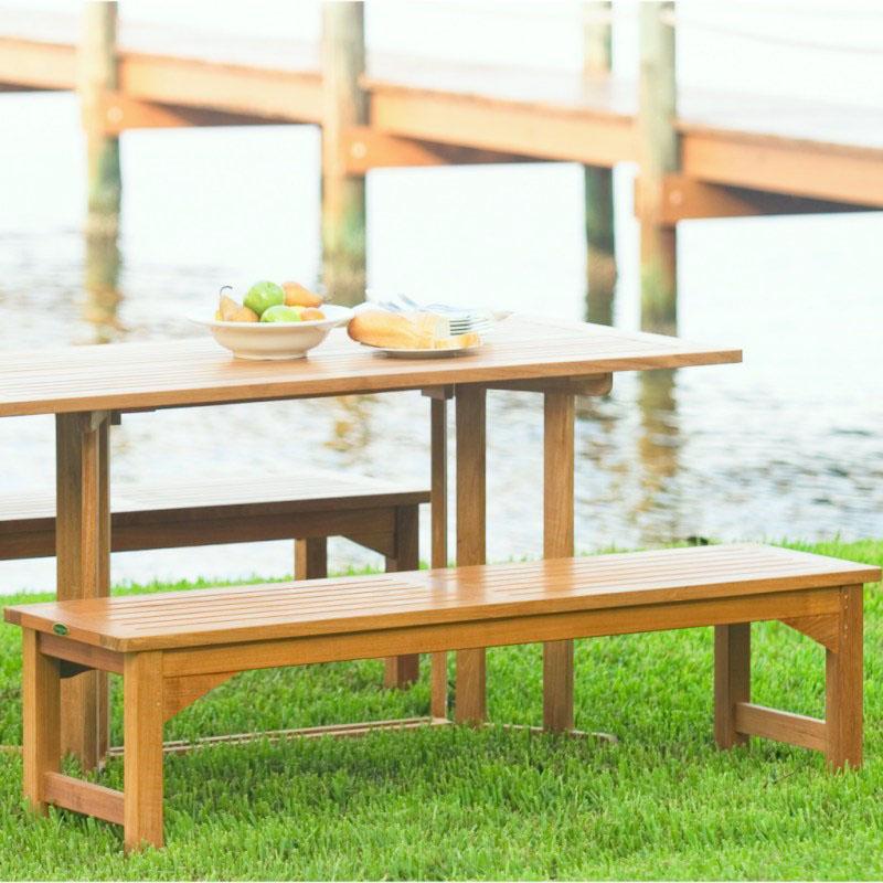 alt="13929 Veranda teak 5 foot long Backless Bench and table with plate of bread and bowl of apples and pears on grass area overlooking boat dock and lake"