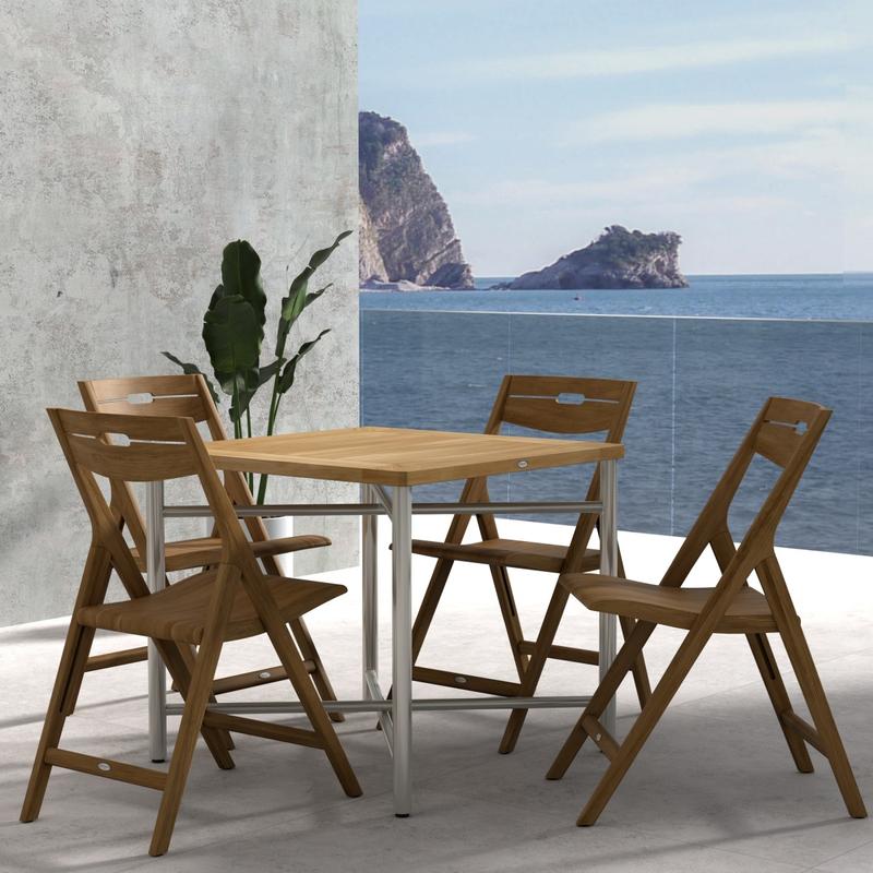 alt="70450 Surf Odyssey Folding Dining Set of Odyssey Bistro Table and 4 Surf Side Chairs in angled side view on a stone patio with the ocean and blue sky in the background"