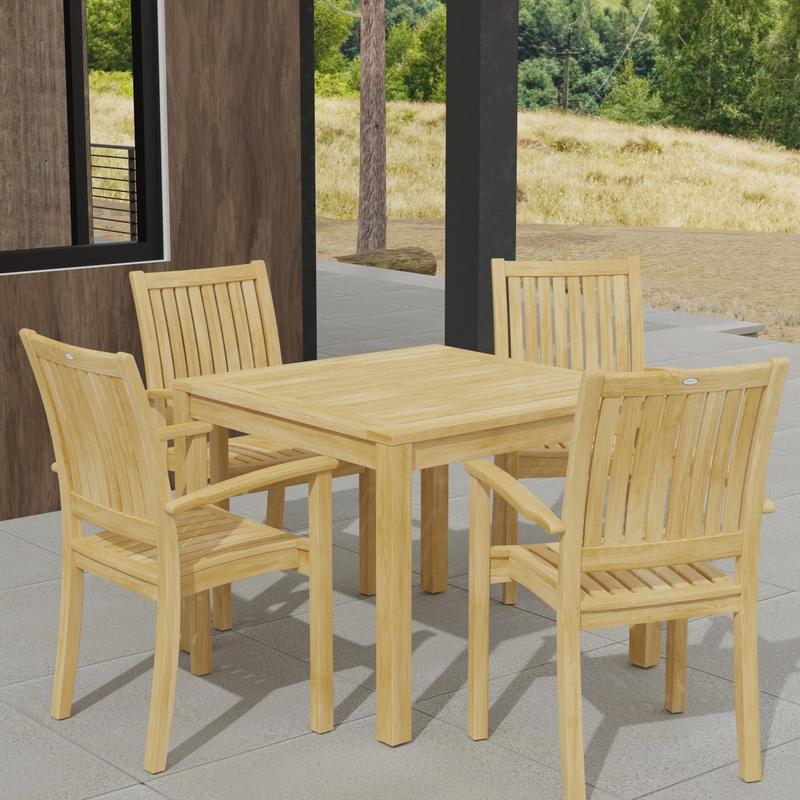 alt="70210 Sussex 5 pc Teak Dining Set of Square Bistro Teak Table and 4 Sussex Armchairs in angled corner view on patio of house next to windows with grass and trees in the background"