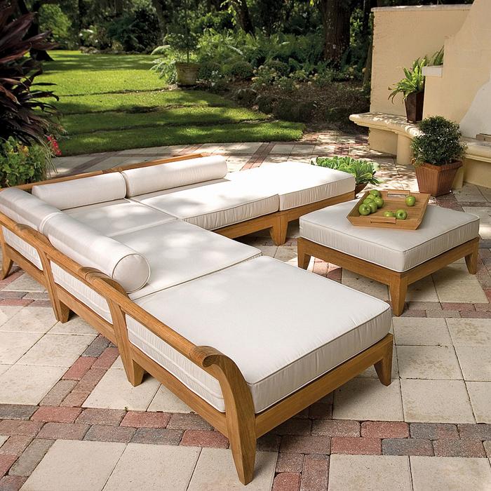 alt="16766 Aman Dais Sectional Set with bolsters and cushions a teak tray with green apples on an ottoman on an outside paver patio with potted plants and a lush background"