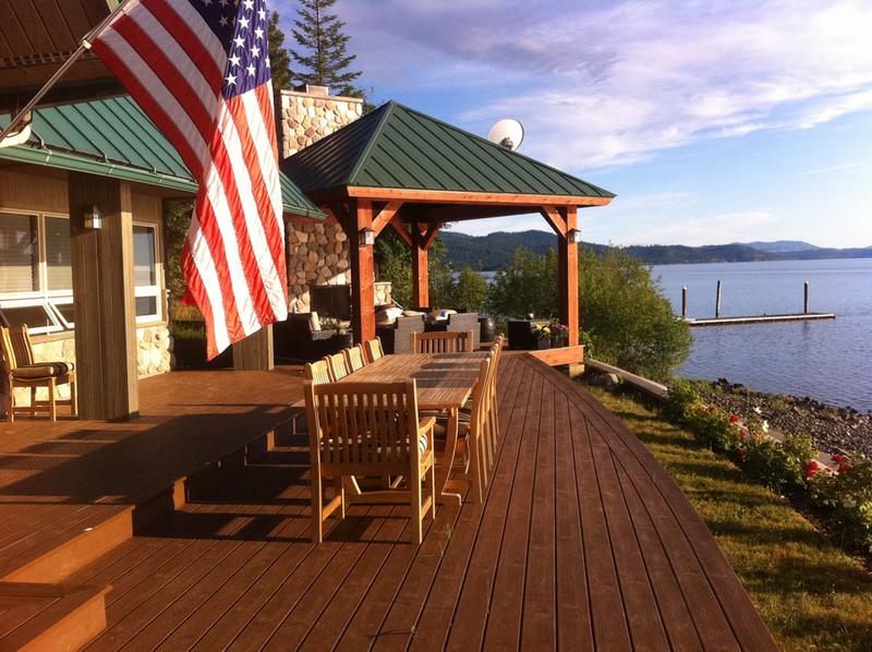 alt="70891 Veranda grand extension table with veranda dining and side chairs on deck by lake with gazebo and US flag"