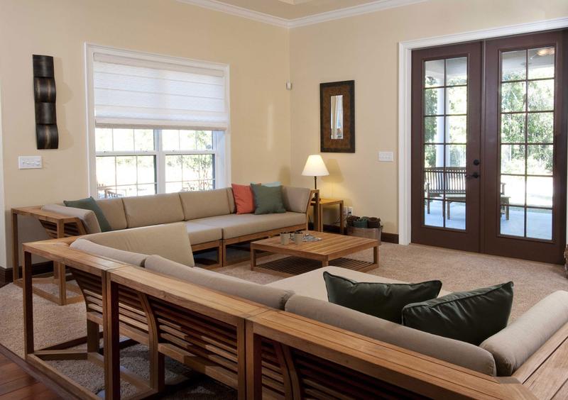 alt="12800 maya teak corner frame with cushions collection set indoors on carpet facing french doors to outdoor patio with landscaped background"