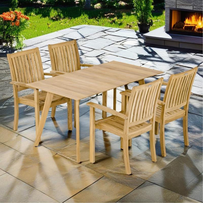 alt="70564 Surf Sussex 5 pc Dining Set of Surf 5ft Rectangular Table and 4 Sussex Dining Chairs angled on stone patio with landscape plants and grass and a lit outdoor fireplace in the background"
