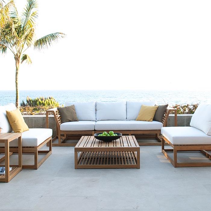 alt=" 70232 Maya 6 piece Sofa Set with cushions front view on outdoor patio coffee table with bowl of green apples a book on bottom shelf of side table with palm tree plants ocean background"