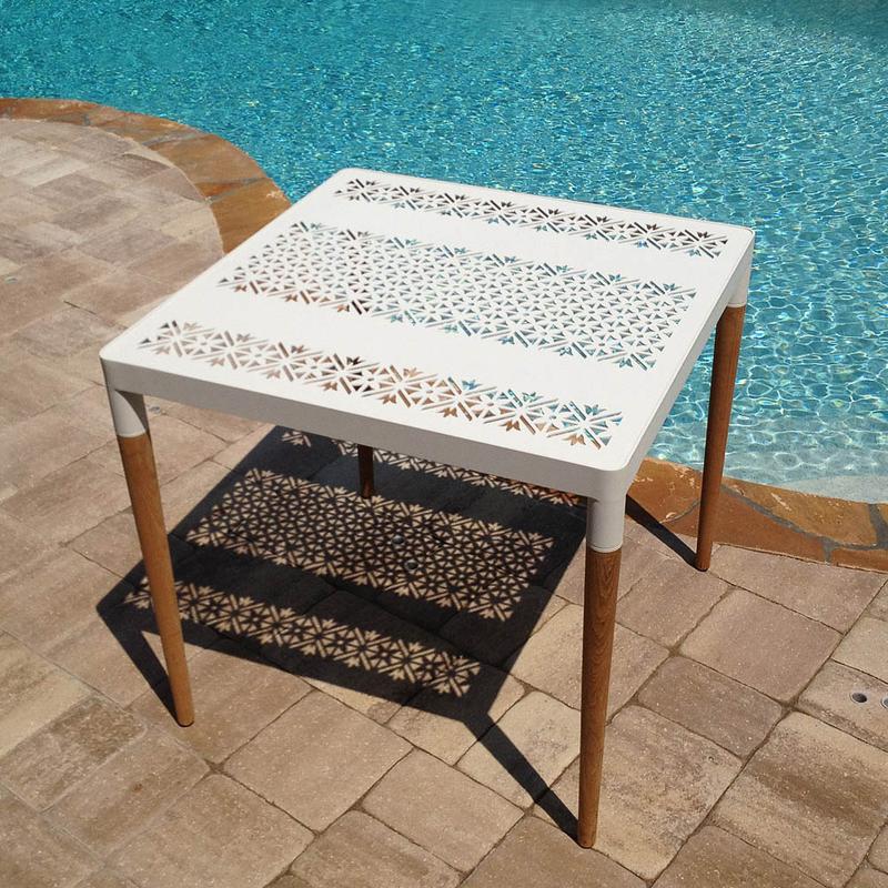 alt="70420 Bloom 32 inch square dining table with glass top angled aerial view on paver deck with pool in background"