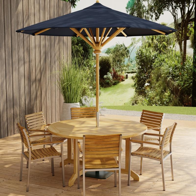 alt="70349 Barbuda Vogue Teak 7 pc Dining Set with optional umbrella on paver patio with wood privacy wall with landscaping plants and trees in background"