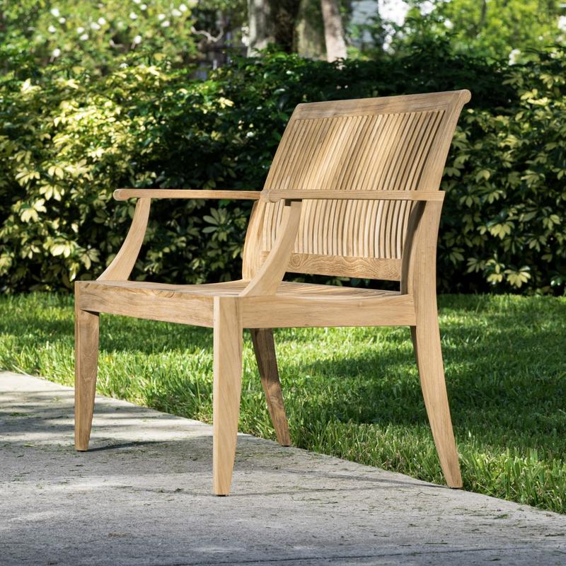 alt="13810 Laguna 4 foot Teak Bench angled on concrete walkway with bushes in background"