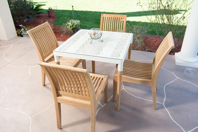alt="70420 Bloom Laguna teak and powder coated aluminum 5 piece Dining Set on stone patio with round glass vase on table center with landscape plants and grass in background"