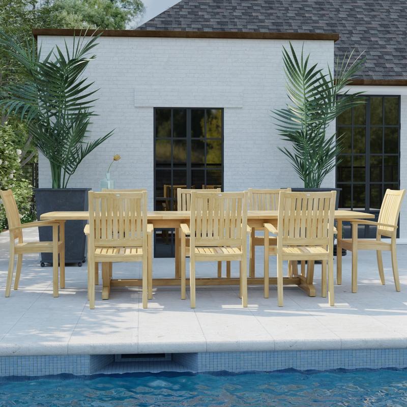alt="70759 Sussex Veranda 9 pc Teak Patio Dining Set in side view on pool deck behind a pool with house with windows and 2 potted plants in background "