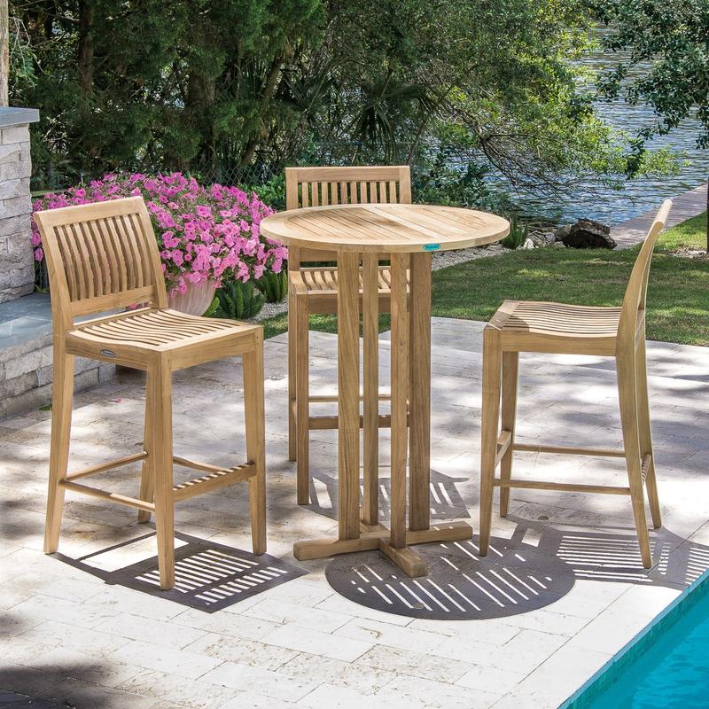 alt="70503 Laguna 4 piece Pub Set on paver patio next to pool and fireplace with flowering plants grass lawn and trees in background with lake view"
