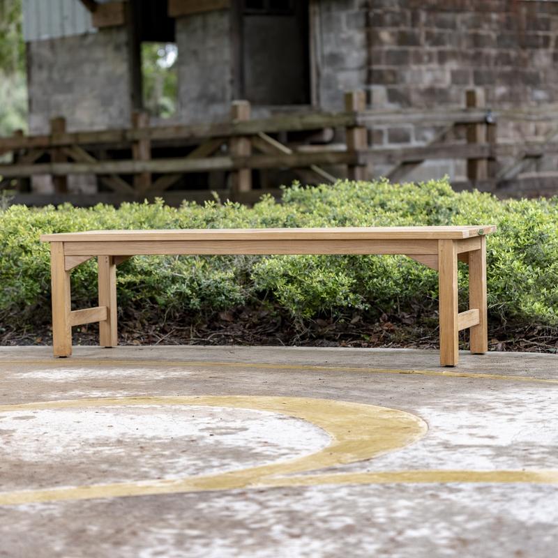 alt="13929 Veranda teak 5 foot long Backless Bench side view on stone patio with bushes and concrete building in background"