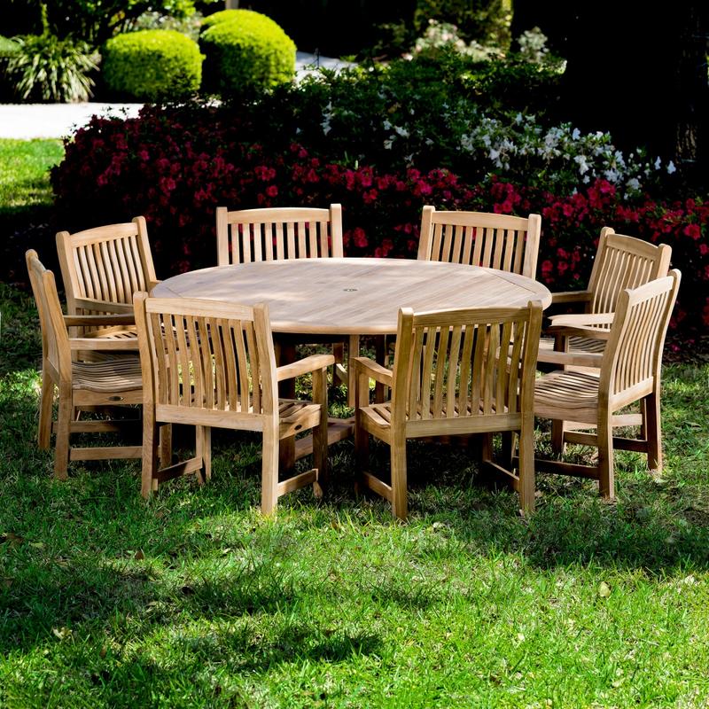 alt="70173 Buckingham 9 pc teak Dining Set with six foot diameter dining table and 8 dining chairs on grass lawn with flowers and tree landscape in background"