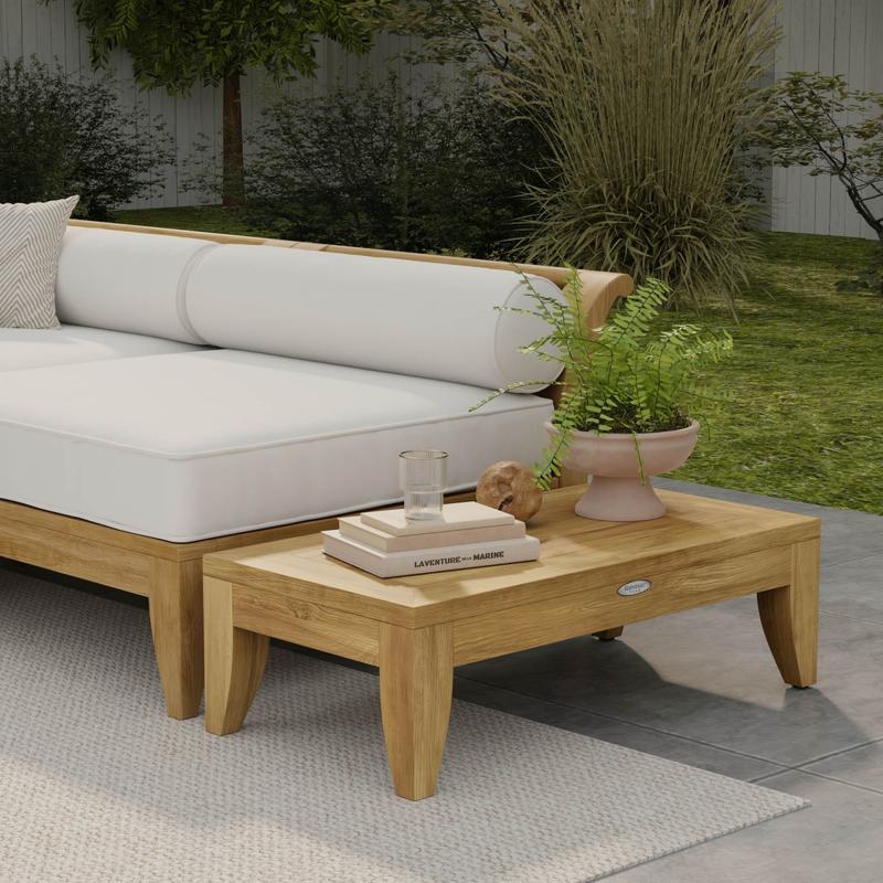 alt="14314 aman dais teak side table next to Aman Dais Sectional with a potted plant and books and glass on top with grass lawn and landscaping plants in background "