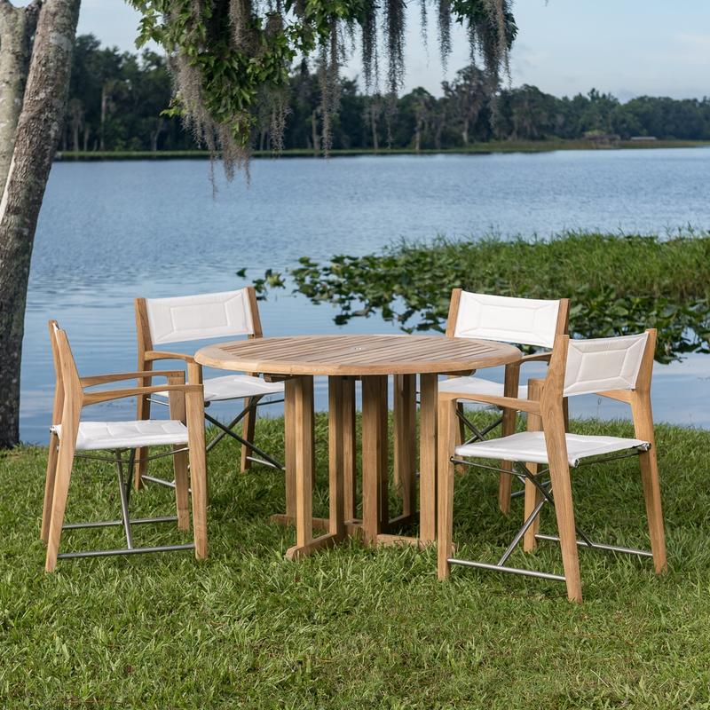 alt="70473 Odyssey Barbuda 5 piece Folding Dining Set of 4 folding director chairs and a 48 inch round teak table on grass with palm trees overlooking blue lake"