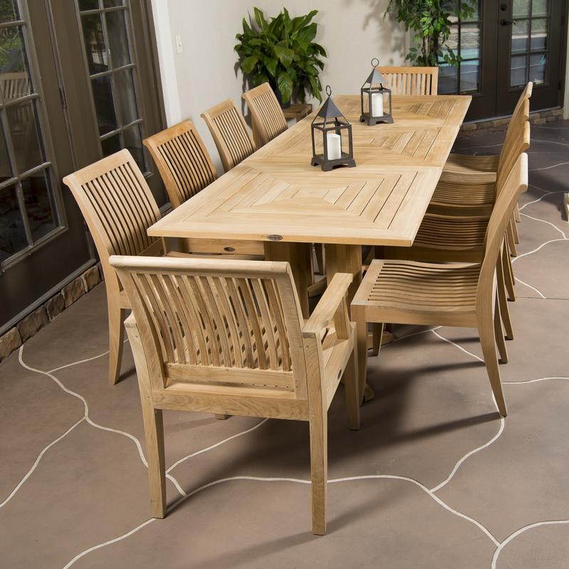 alt="70434 Pyramid teak Rectangular Table Dining Set showing 2 black metal pillar candle holders with white candles on table on stone patio 2 potted trees end angled view with house in back "