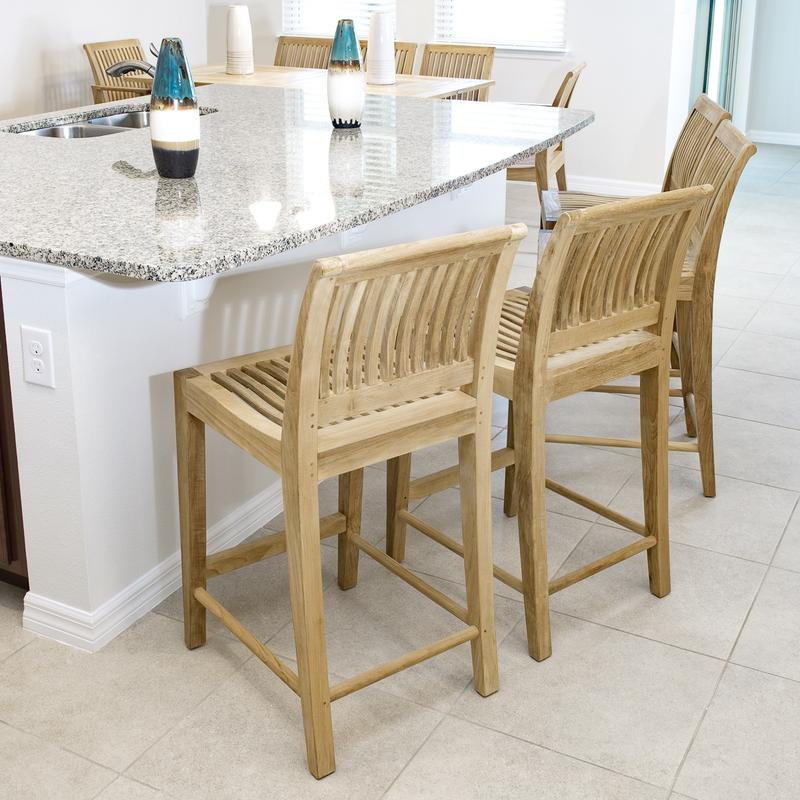 alt="70760 Laguna Teak Counter Stools Set of 4 showing four on tile floor in aerial angled view against slate tile kitchen counter with two blue striped vases a dining table set and wall in background"