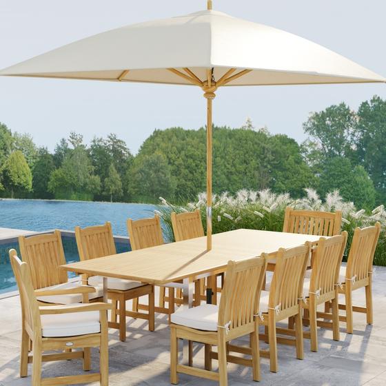 70826  Vogue Veranda 13 pc Teak Dining Set with optional seat cushions and umbrella showing angled end view on patio next to a pool with plants and a lake with trees in background