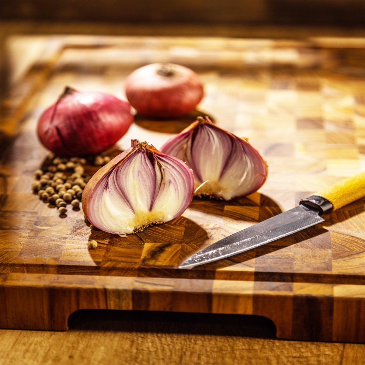 19124 Butcher Block 20 inch Rectangle Charcuterie Cutting Board on a countertop showing closeup angled view with red onions and knife on top