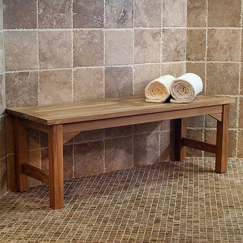 alt="13940 Veranda 4 foot Teak Backless Bench angled view against a tiled wall shower area with 2 rolled white towels on top of bench"