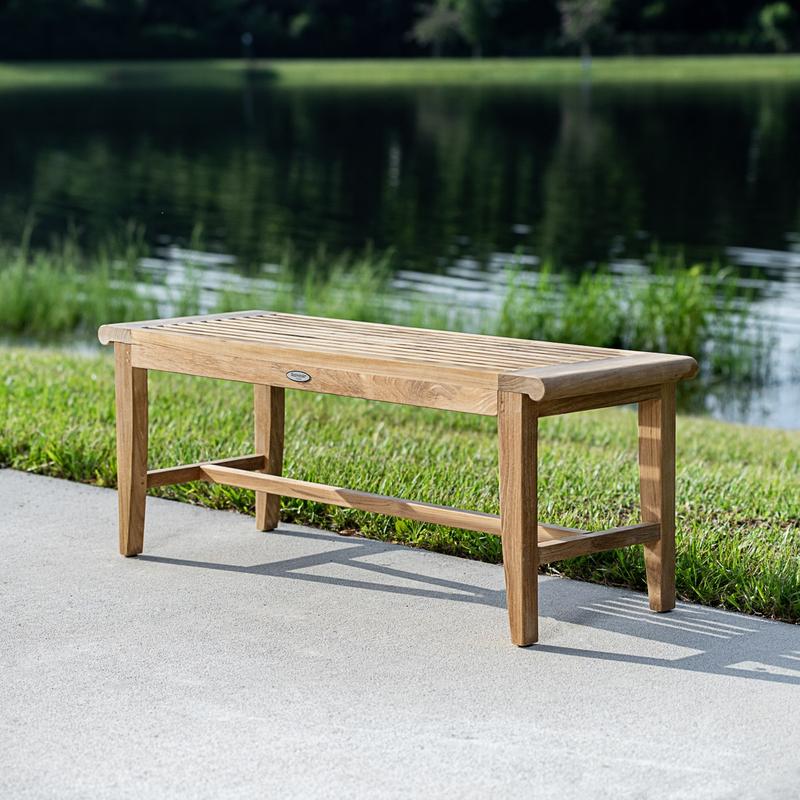 alt="13915 Laguna 4 foot long teak Backless Bench on concrete walkway with grass and lake in background"