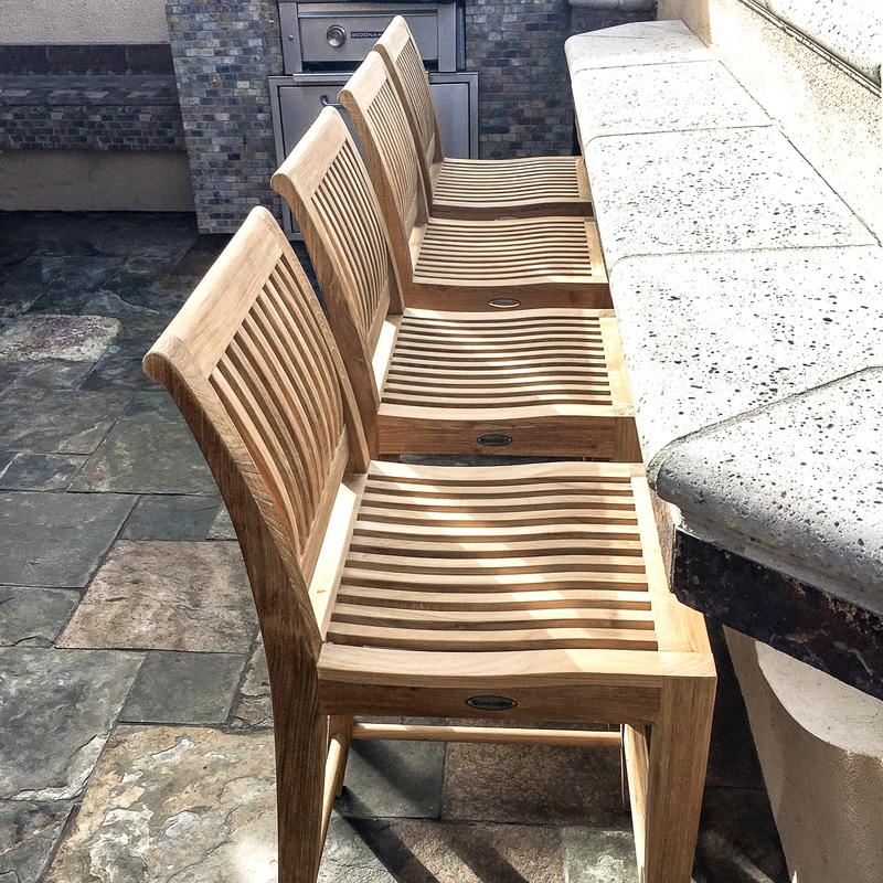 alt="70760 Laguna Teak Counter Stools Set of 4 showing closeup view on tiled stone patio against a slate tile counter with an outdoor kitchen in the background"