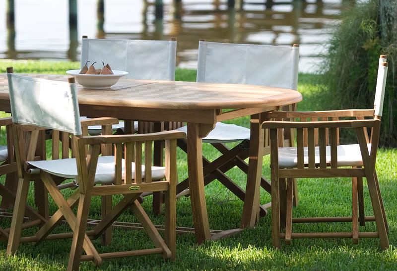 alt="70015 Montserrat Director 9 piece teak Dining Set with white bowl of pears on grass lawn with boat dock and lake background"