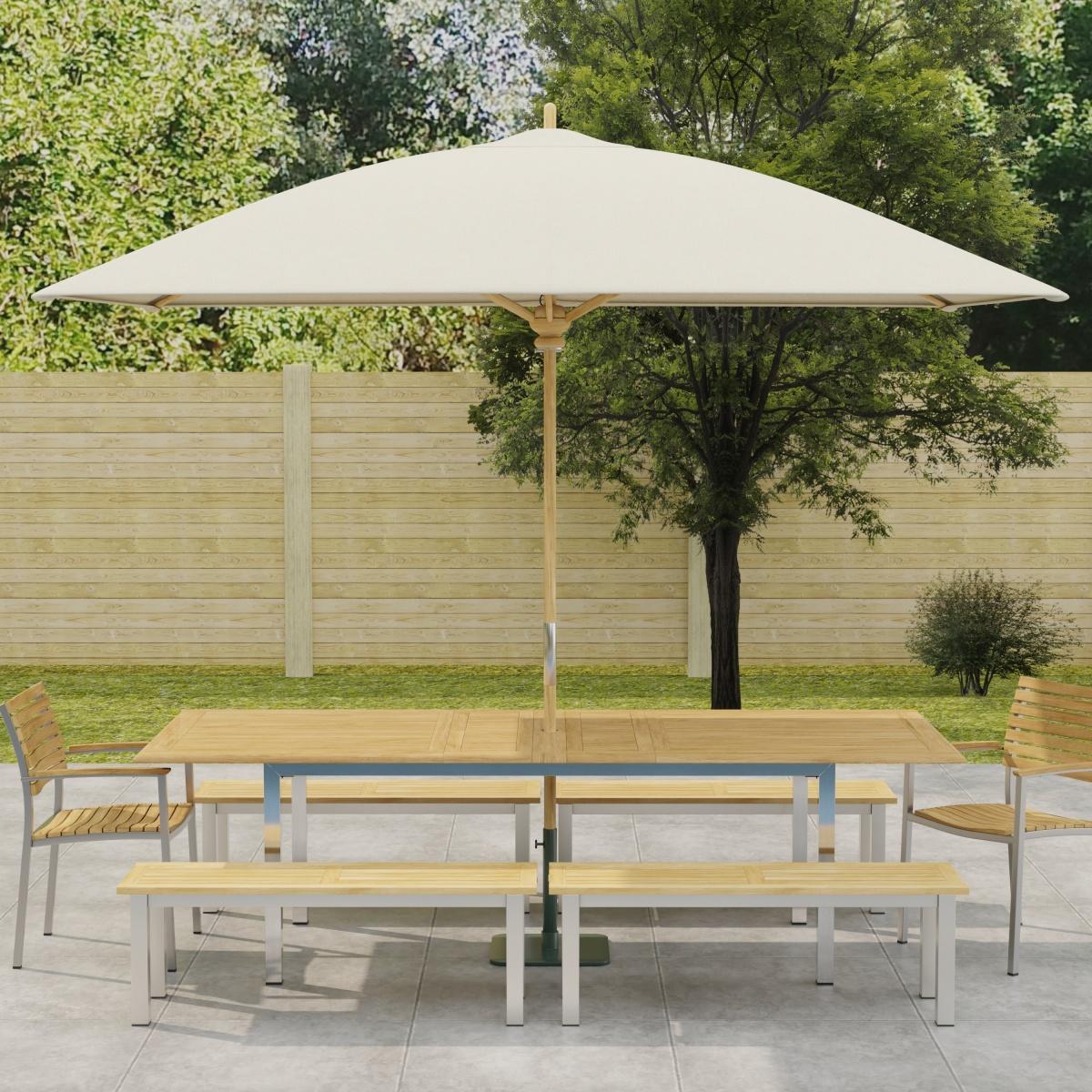 70440 Vogue 7 piece Teak and Stainless Steel Picnic Set with optional umbrella in side view in front of a pool with landscape plants and trees in the background