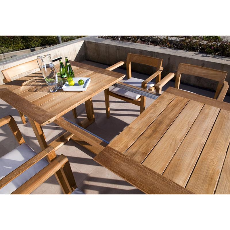 alt="70299 Horizon teak 7 piece Dining Set with 3 sparkling water bottles a water pitcher and limes on plate showing table expanded on concrete terrace"