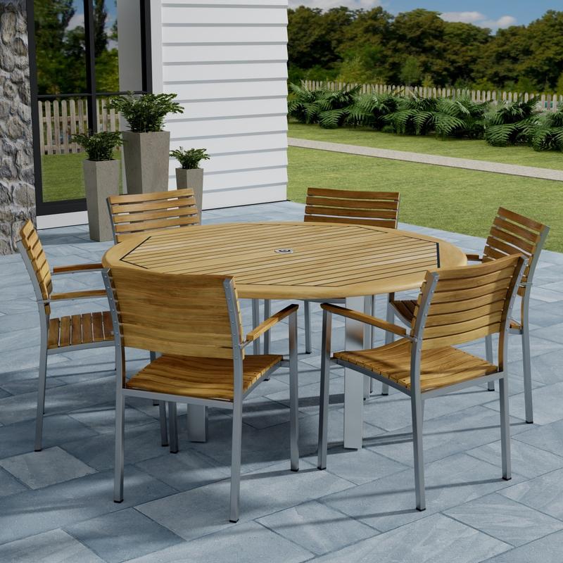 alt="70442 Vogue Teak 7 pc Dining Set showing Vogue 60 inch Round Dining Table and 6 Dining Chairs angled side view on patio with window and fence with trees in background "