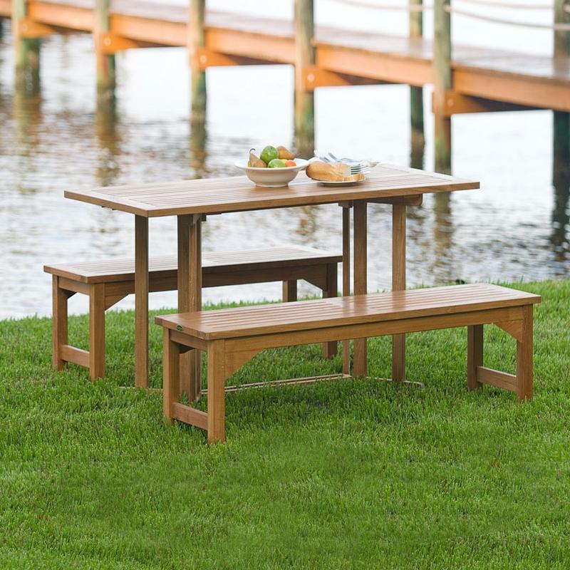 alt="70061 Barbuda Picnic Table teak Dining Set white bowl of whole fruit and plate of french bread on table on grass field with lake and dock in background"