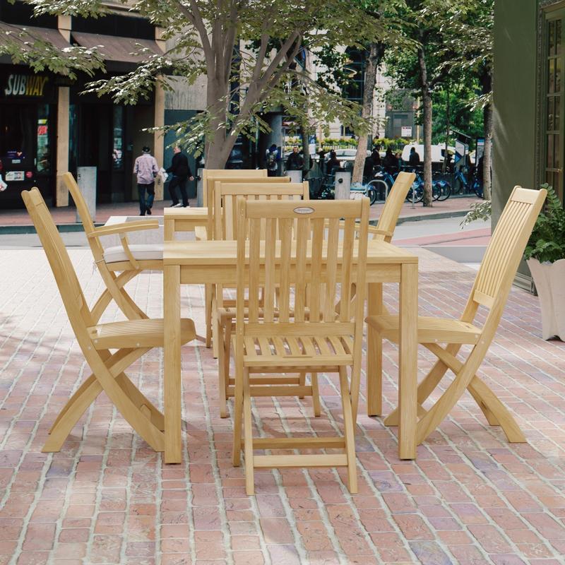 alt="70570 Barbuda 5 pc Dining Set of Barbuda Bistro Teak 36 inch Square Dining Table and 4 Barbuda Folding Chairs side angled view on brick paver courtyard with buildings and trees and people walking in background"