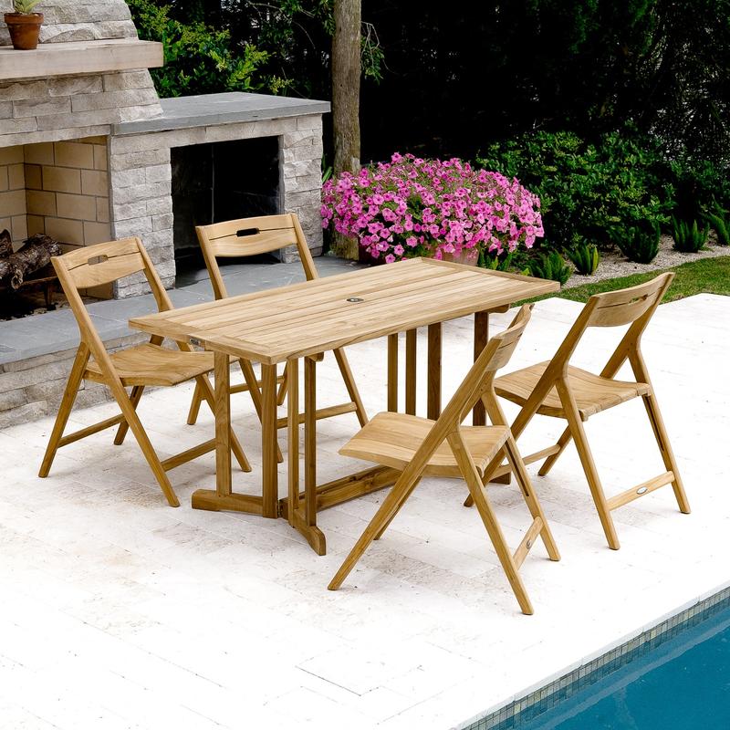 alt="70475 Surf Nevis 5 piece teak rectangular Dining Set on pool patio with flowering plant next to fireplace shrubs and trees in background"